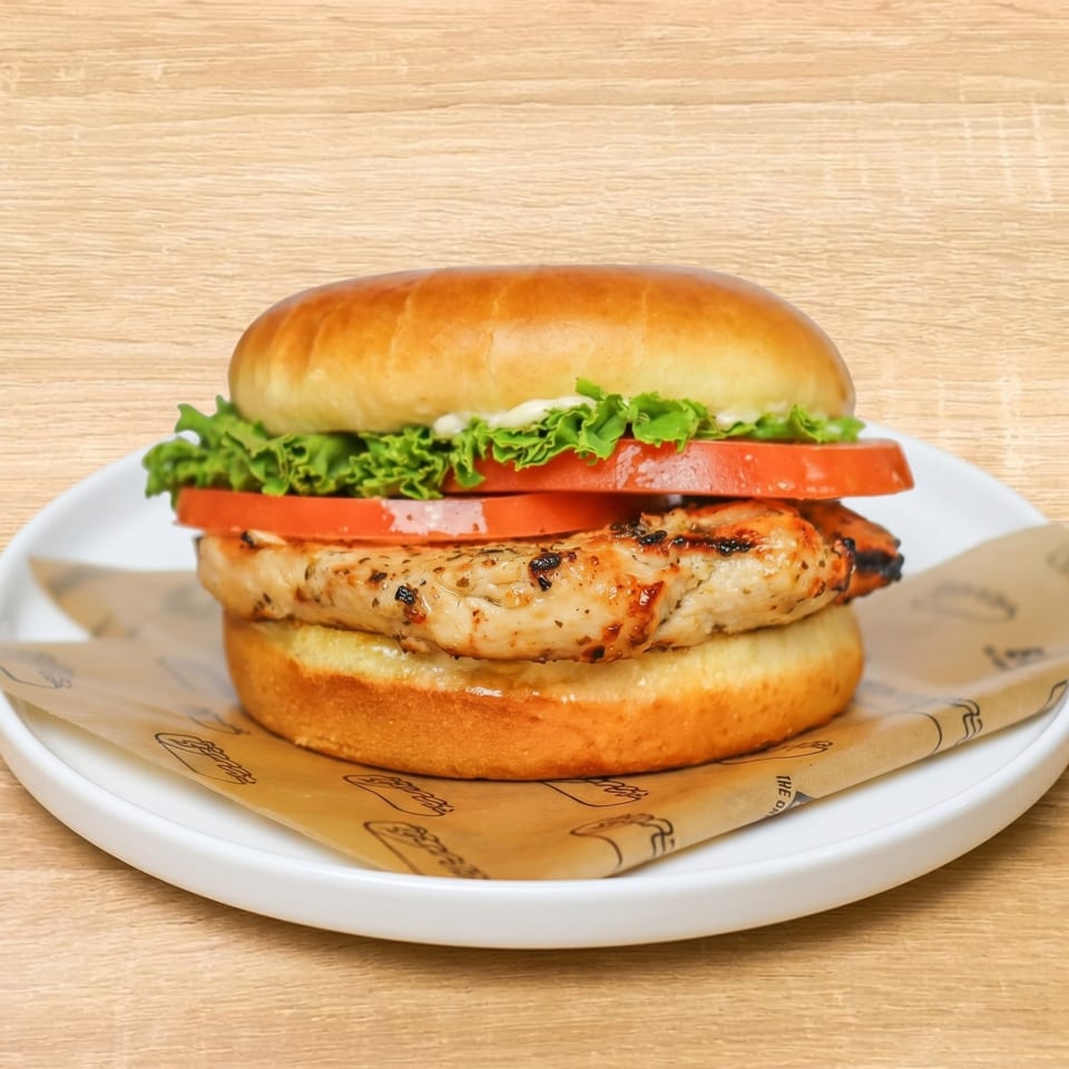 Grilled chicken sandwich with lettuce, tomato, and mayonnaise on a brioche bun, served on a white plate.